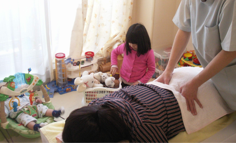 赤ちゃんと女の子がキッズルームで遊んでいる中で治療を受けるお母さん